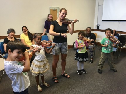 image of teacher with small children playing violins