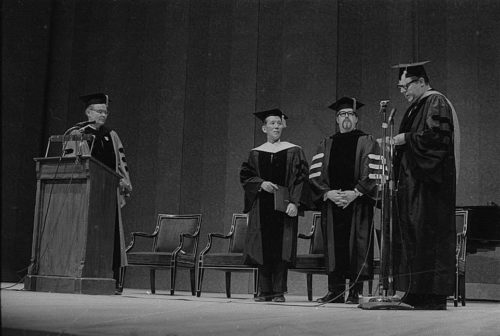 Conferral of an honorary doctoral degree on Shinichi Suzuki. Professor Donald Shetler hoods the newly named Dr. Suzuki; University President Robert Sproull stands at far left, and ESM Director Walter Hendl stands at far right.