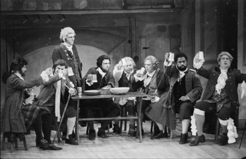In the tavern in act I. The eight men on-stage are Parchment (standing), Raccoon (second from right), Washball (far right), and the rest, in no particular order, are Jack Rattletrap, Quadrant, Hum, Trushoop, and McSnip. Parchment, Hum, Quadrant, and Rattletrap are the four so-called Humorists who devise a cunning trap b which to exploit others for gain.